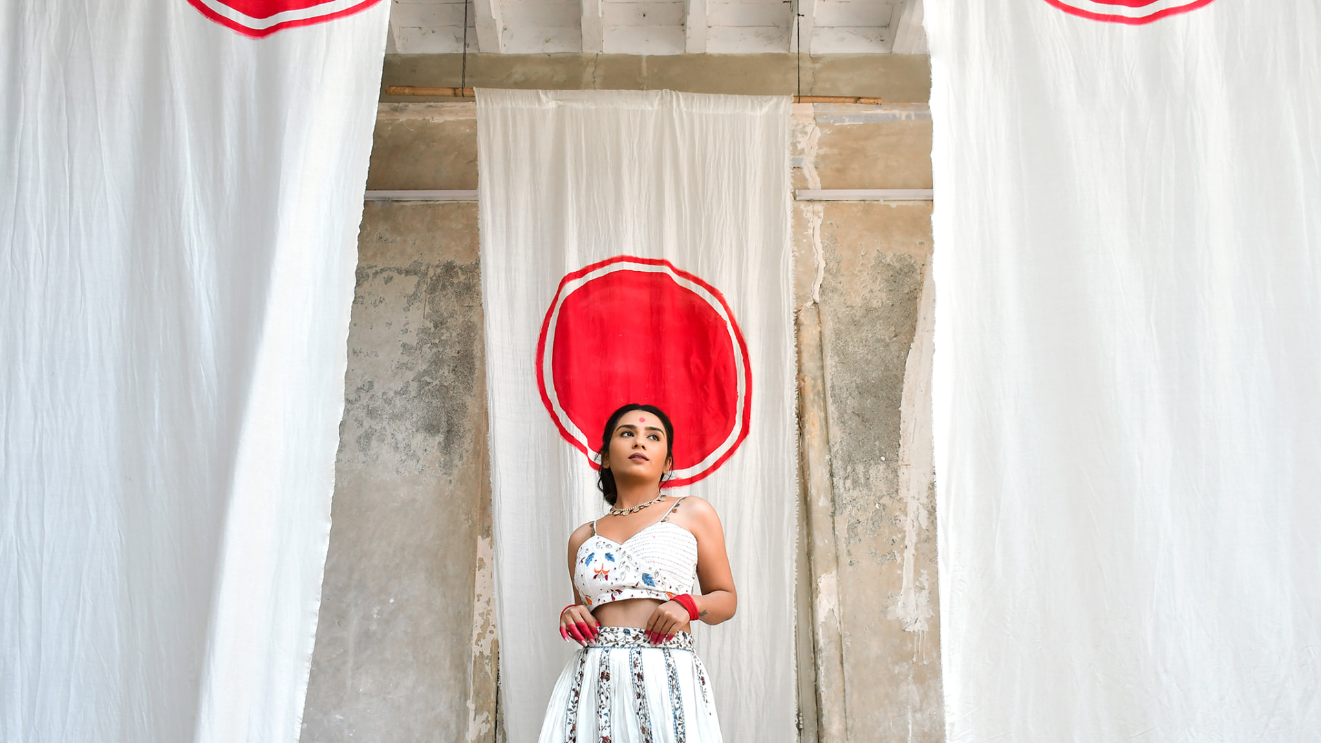 Model in ivory embroidered crop top and skirt before a red sun backdrop