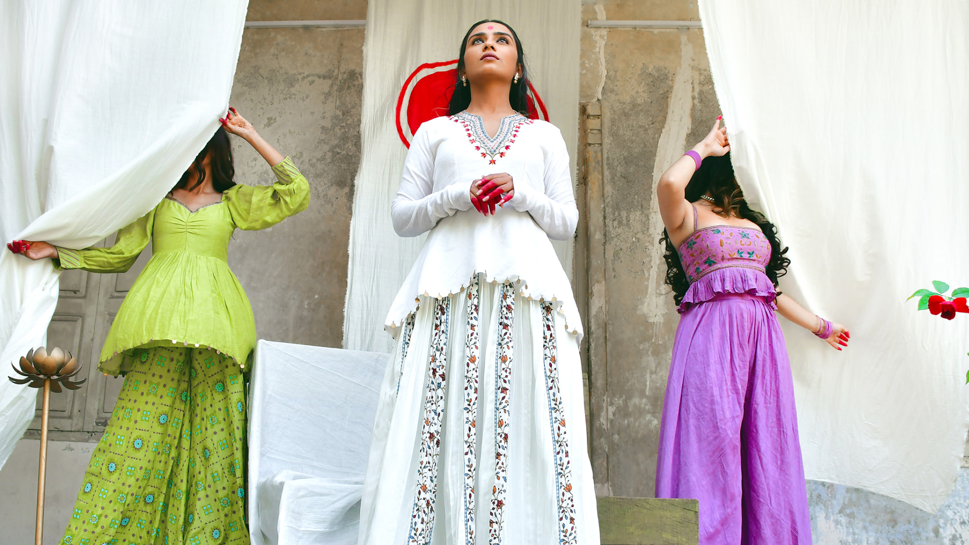 Three models in white, purple and green traditional outfits